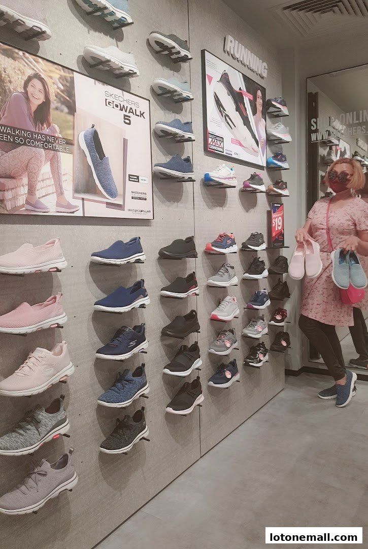 A woman poses with Skechers shoes displayed on a wall, showcasing various styles.
