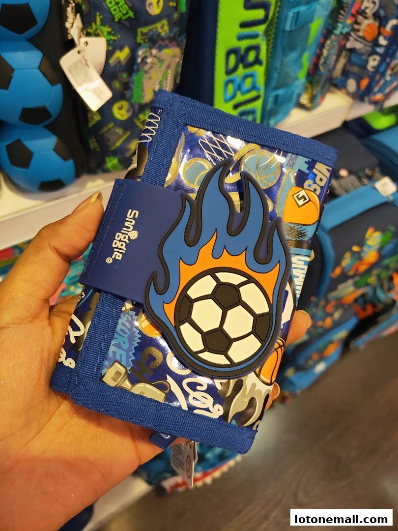 A hand holds a Smiggle wallet featuring a soccer ball with flames design.