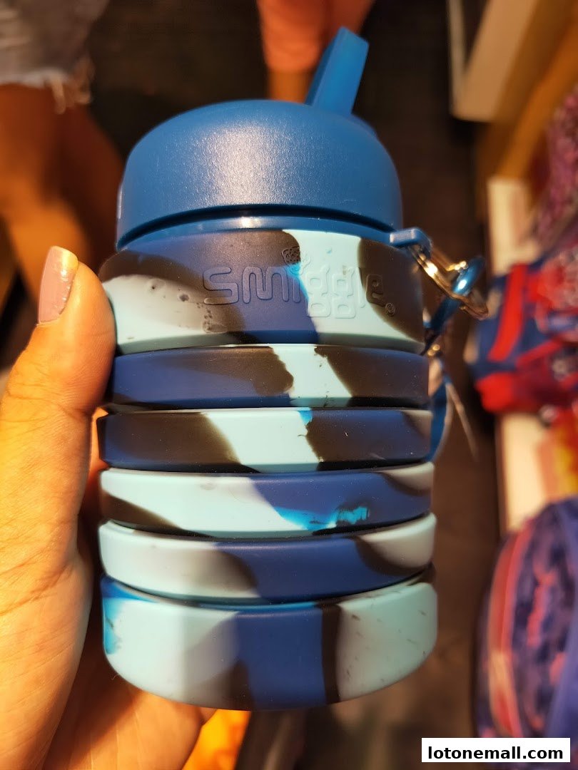 A hand holds a blue and black camouflage Smiggle water bottle with a straw lid.