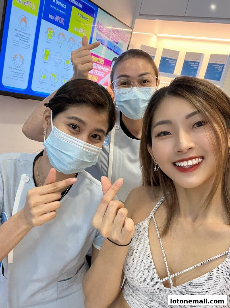 Three smiling women in medical attire pose for a selfie, showing heart gestures.