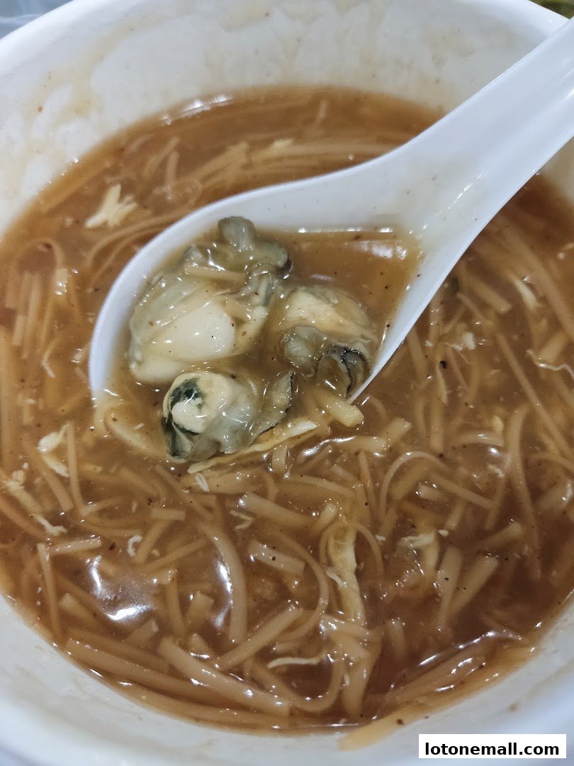 A close-up shot of a bowl of oyster mee sua with a spoon lifting some oysters.