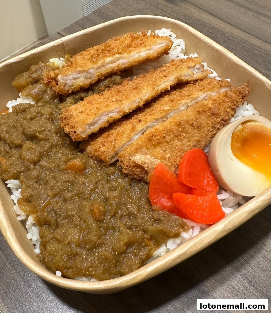 A delicious bowl of Japanese curry with crispy katsu, rice, pickled radish, and a soft-boiled egg.