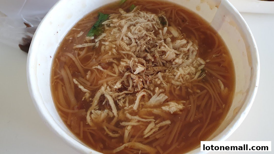 A close-up shot of a bowl of noodle soup with shredded chicken and herbs.