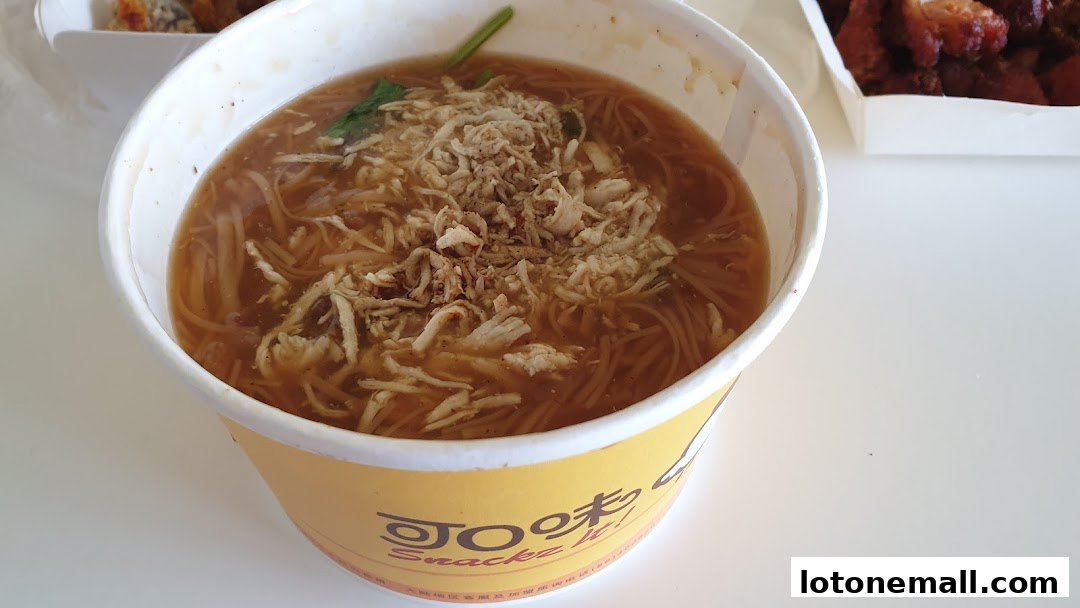 A close-up of a bowl of noodle soup with shredded chicken and crispy toppings.