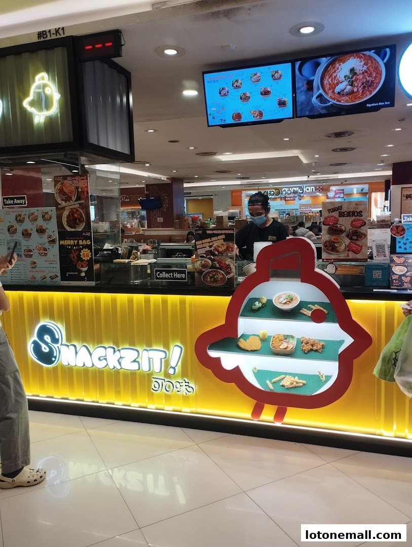 A bright yellow Snackz It! shop counter with food displays and digital menus above.