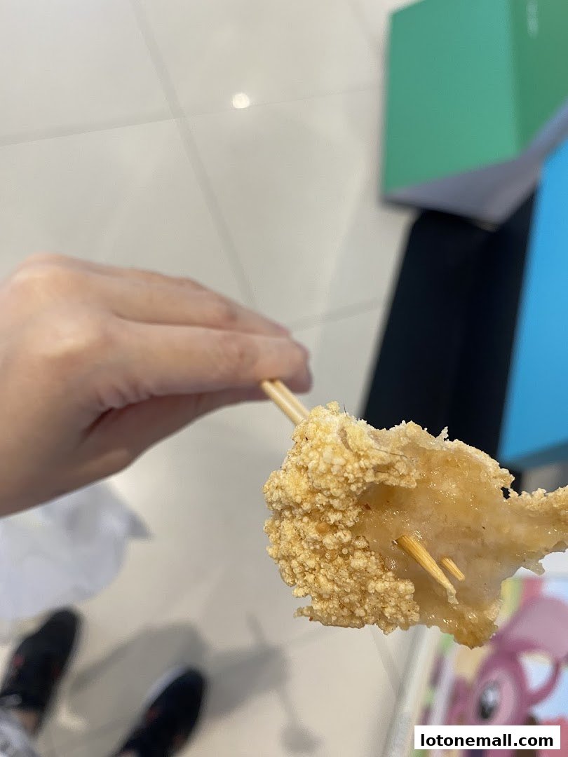 A hand holds a crispy, deep-fried snack on a skewer.