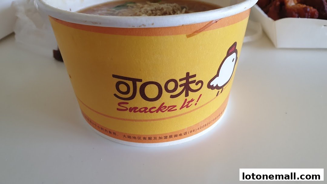 A close-up of a yellow cup with the Snackz It! logo and a cartoon chicken.