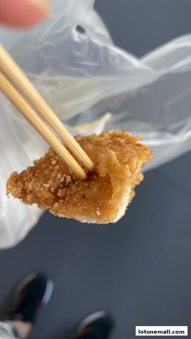 A close-up of fried chicken being held by chopsticks, with a hair visible.