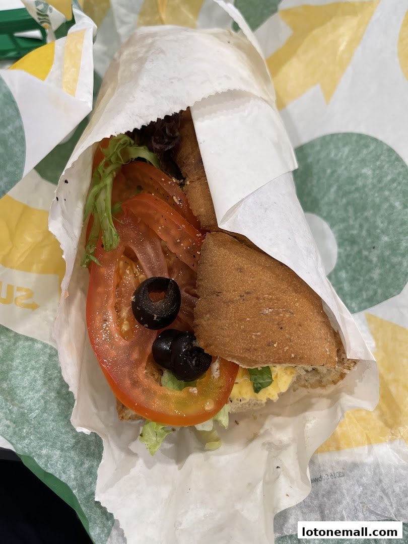 A close-up of a Subway sandwich with fresh lettuce, tomatoes, and olives.