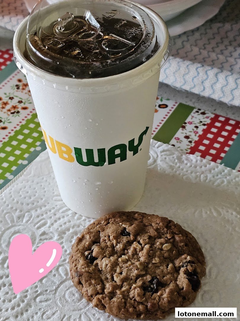 A Subway branded cup of iced beverage next to a cookie on a napkin.