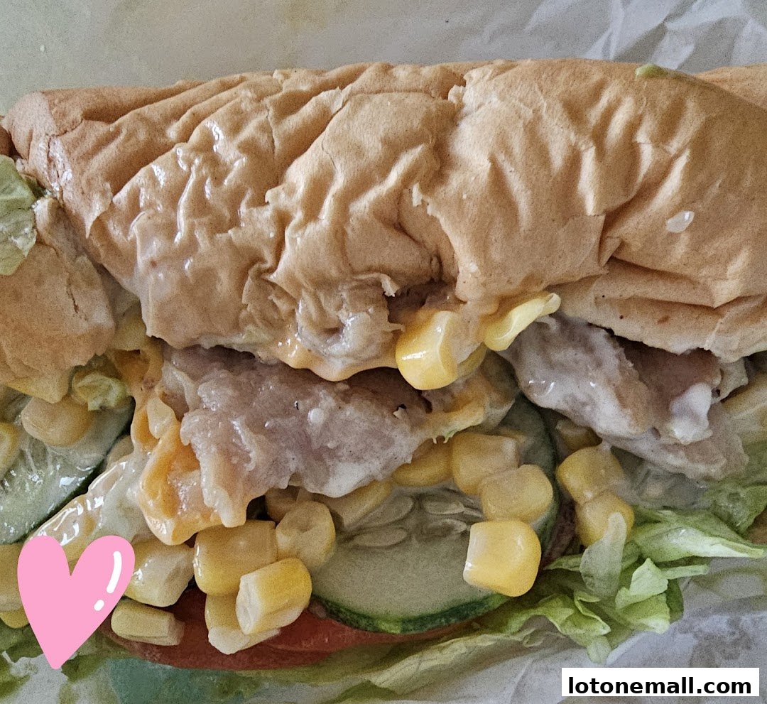 A close-up shot of a delicious Subway sandwich filled with meat, corn, cucumber, and sauce.