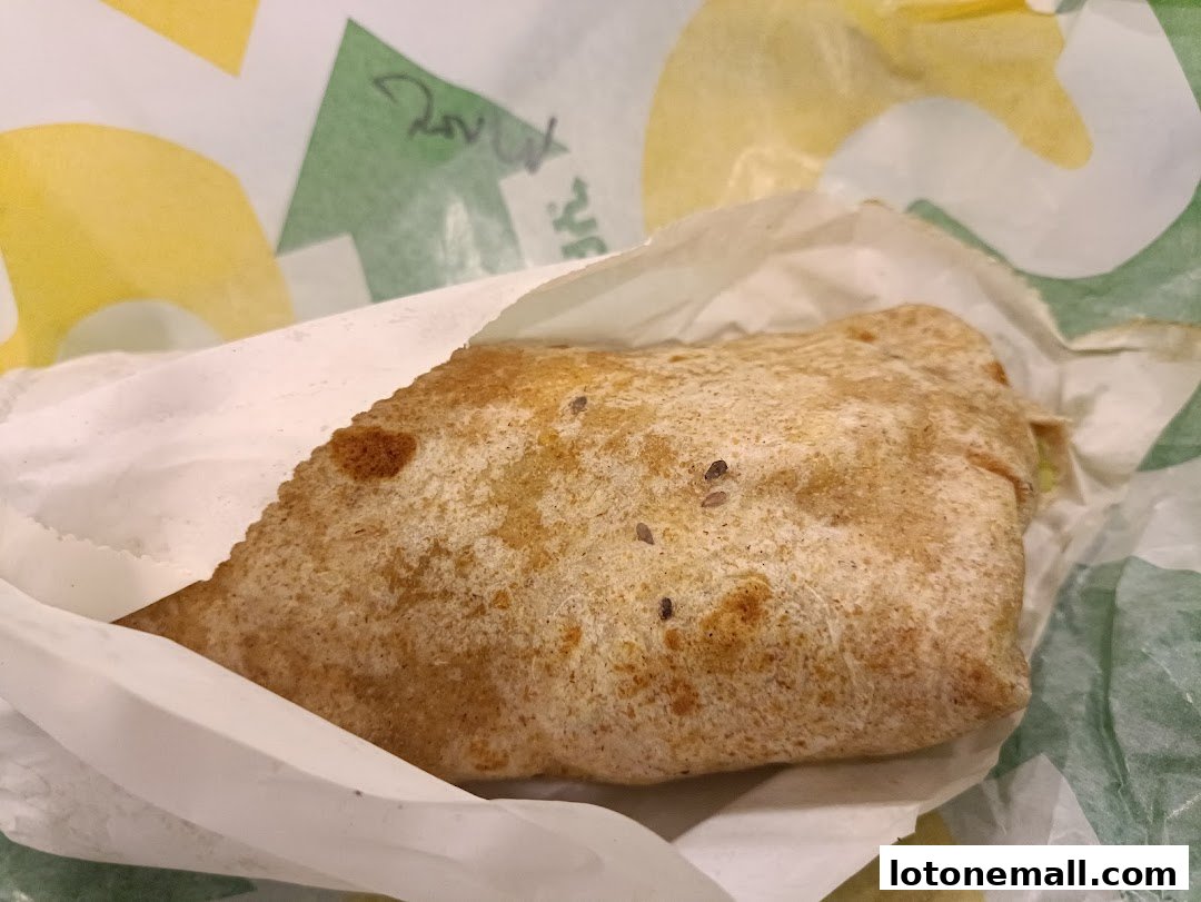A close-up of a Subway wrap, partially unwrapped, with the brand's signature paper.