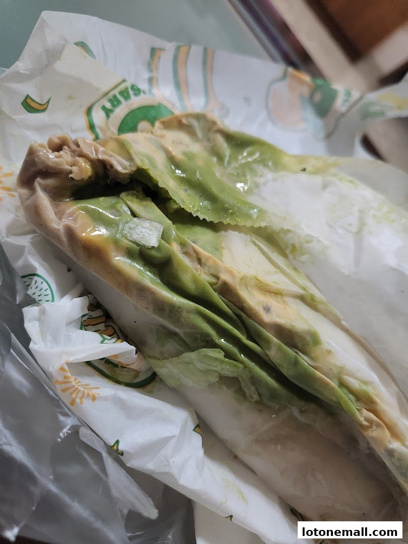 A close-up of a Subway sandwich with lettuce and sauce, wrapped in branded paper.