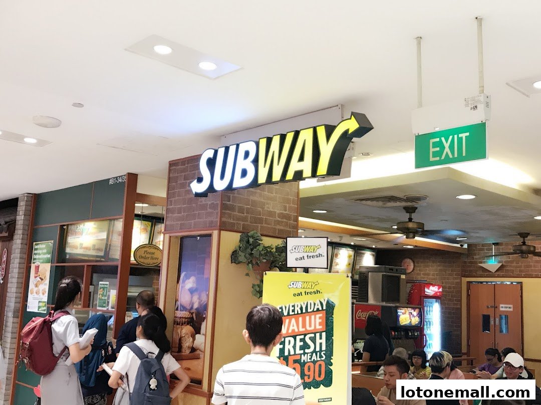 People queuing at a Subway restaurant with prominent signage and a menu board.