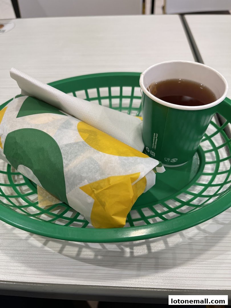 A Subway sandwich and a cup of tea served in a green basket on a white table.