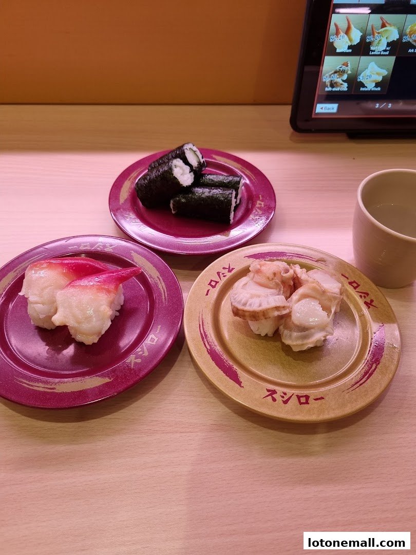 Plates of sushi and a cup on a wooden table, with a tablet displaying menu items in the background.