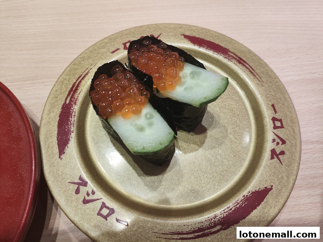 Two pieces of sushi with cucumber and salmon roe on a decorative plate.