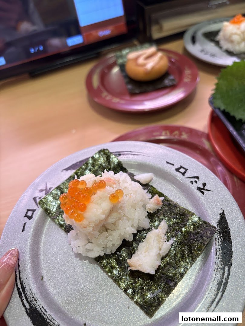 Close-up of sushi on a conveyor belt with other plates in the background.