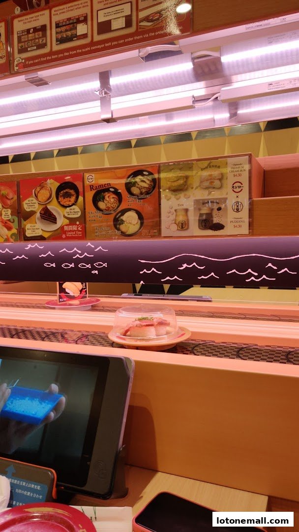 A conveyor belt sushi restaurant with various dishes displayed on the belt and menu boards above.