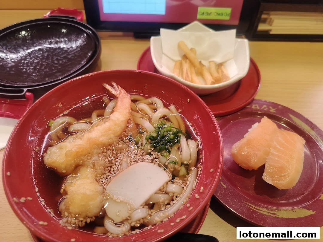 A bowl of udon noodles with tempura shrimp and a plate of salmon sushi.