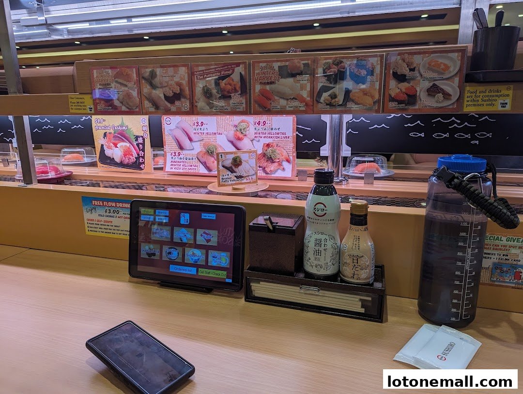 A sushi conveyor belt restaurant with a tablet ordering system and various sushi dishes displayed.