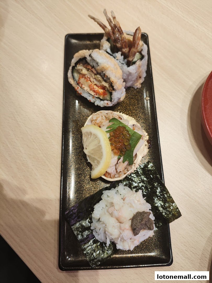 A black rectangular plate holds three different sushi preparations, including rolls and a crab shell dish.