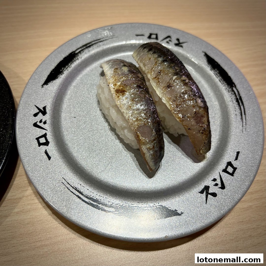 Two pieces of grilled mackerel sushi on a plate with Japanese text.