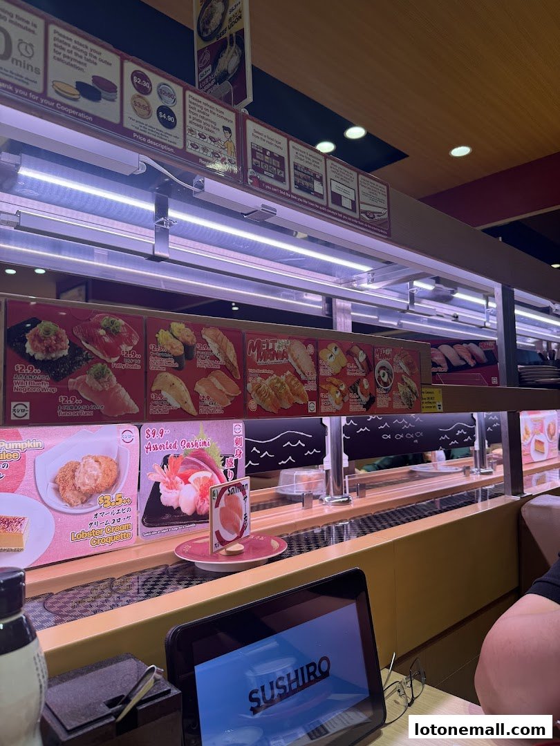 A conveyor belt sushi restaurant with various sushi dishes displayed on a screen.