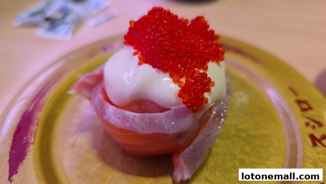 A close-up of a sushi roll topped with mayonnaise and red roe on a golden plate.