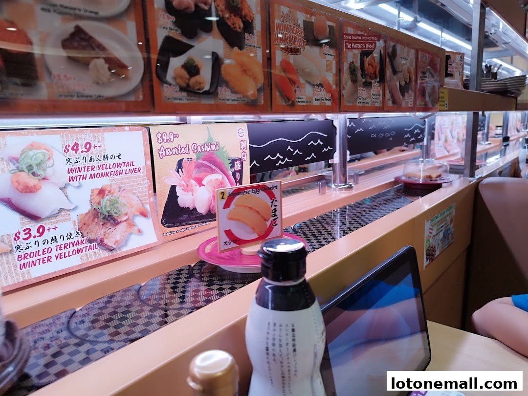 A conveyor belt sushi restaurant with various sushi dishes displayed on a screen and on the belt.