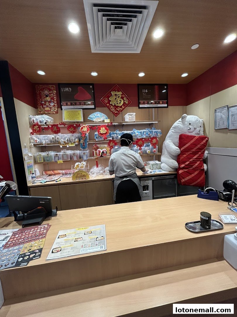 A sushi restaurant counter with a staff member, decorations, and a large plush toy.