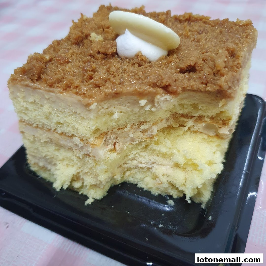 A slice of layered cake with cream and crumb topping, garnished with white chocolate.