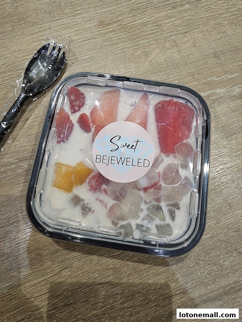 A container of dessert with fruits and jelly, accompanied by a spoon.
