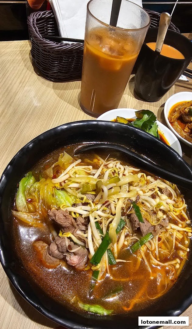 A steaming bowl of beef noodle soup with bean sprouts and cabbage, served with iced tea.
