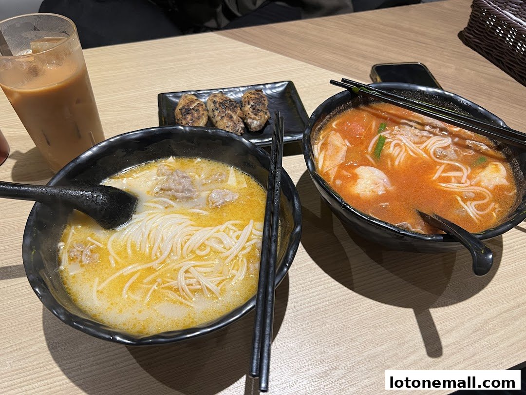 Two bowls of noodle soup, grilled items, and a drink on a wooden table.