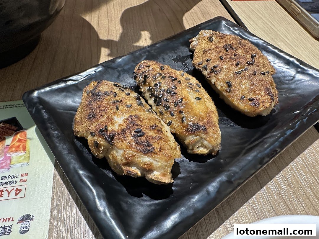 Three crispy chicken wings seasoned with sesame seeds served on a black plate.