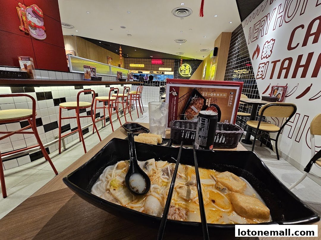 A bowl of noodle soup is served at a table in a brightly lit restaurant with red bar stools.