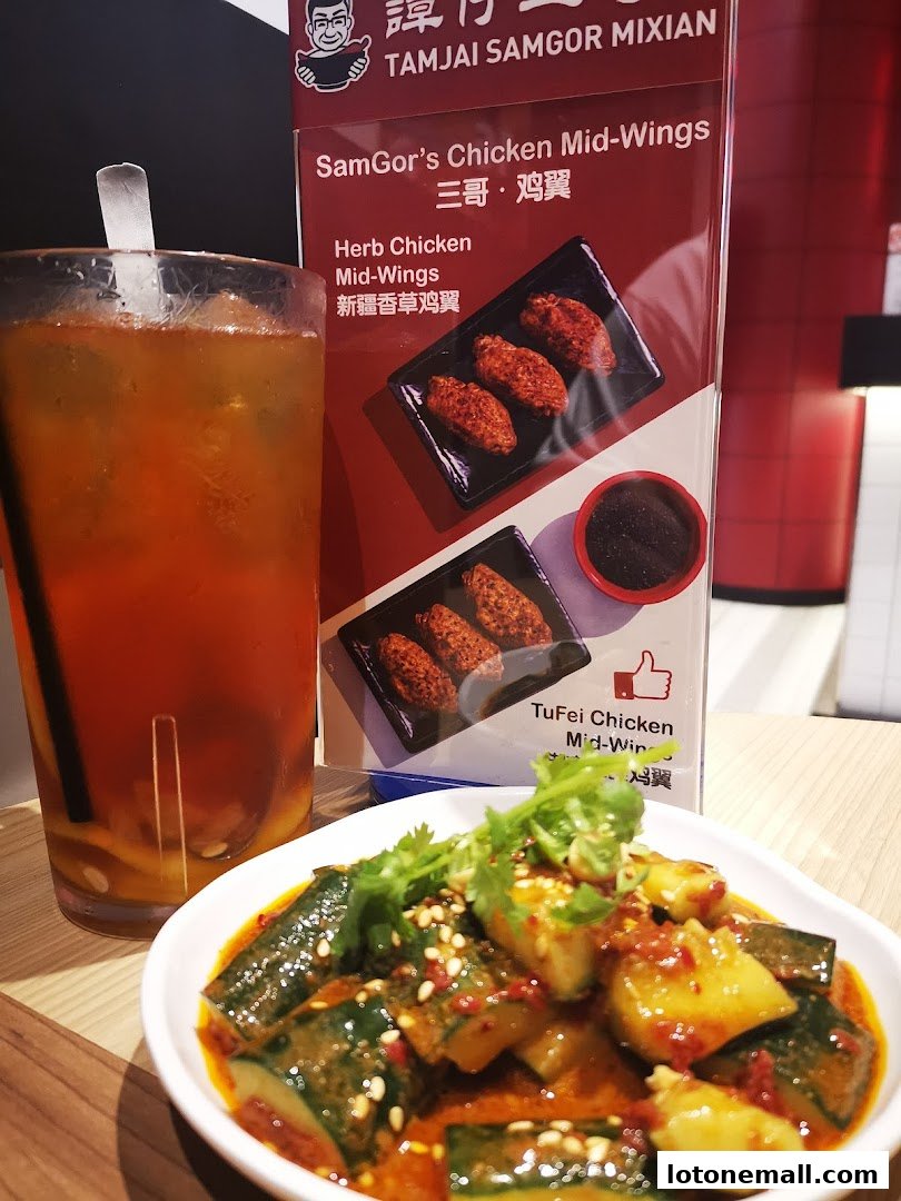 A glass of iced tea and a dish of spicy cucumbers next to a menu featuring chicken wings.