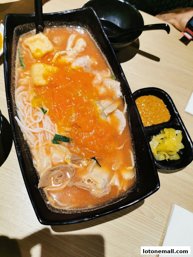 A close-up of a steaming bowl of mixed noodles with meat and tofu in a spicy broth.