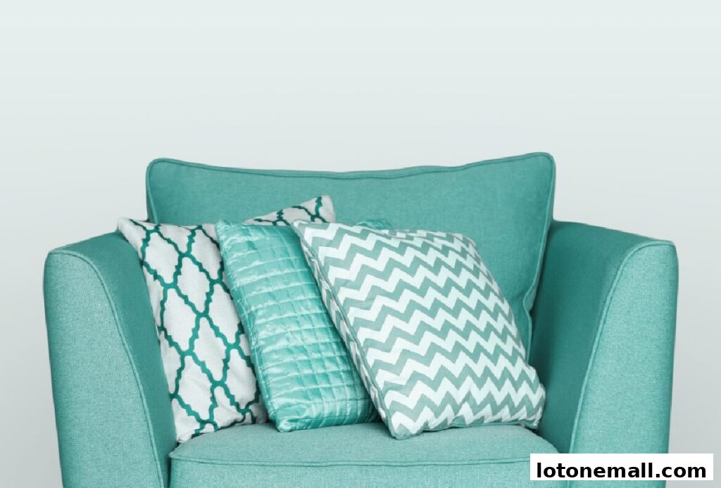 A teal armchair is adorned with three decorative throw pillows in various patterns and textures.