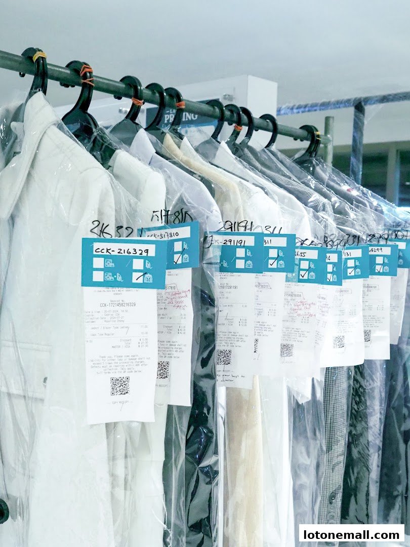Garments on hangers in plastic bags with receipts attached at a laundry service.