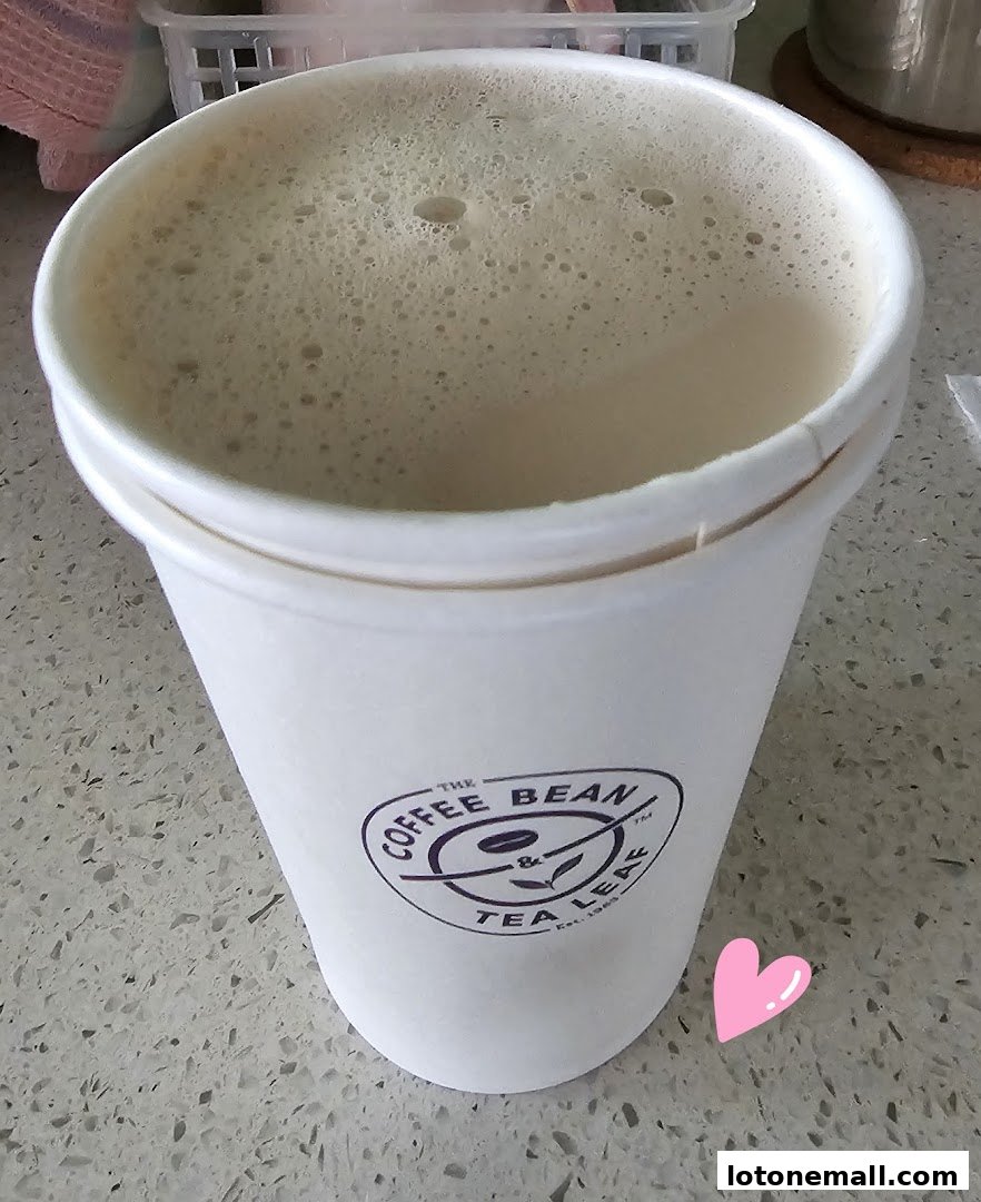 A close-up of a frothy beverage in a white cup with The Coffee Bean & Tea Leaf logo.