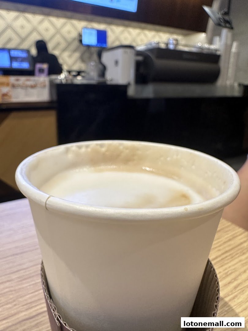A close-up of a steaming cup of coffee with latte art, with a coffee shop counter in the background.