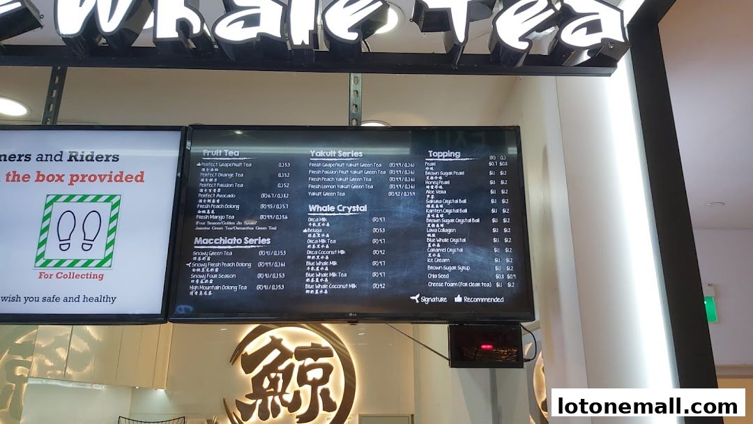 A digital menu board displaying various fruit teas, Yakult series, Macchiato series, and toppings at The Whale Tea.
