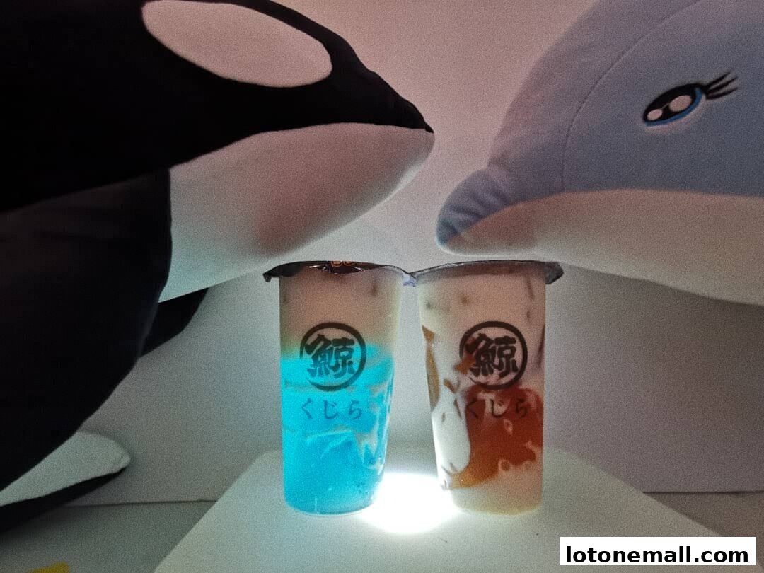 Two bubble tea drinks are displayed between plush whale and dolphin toys.