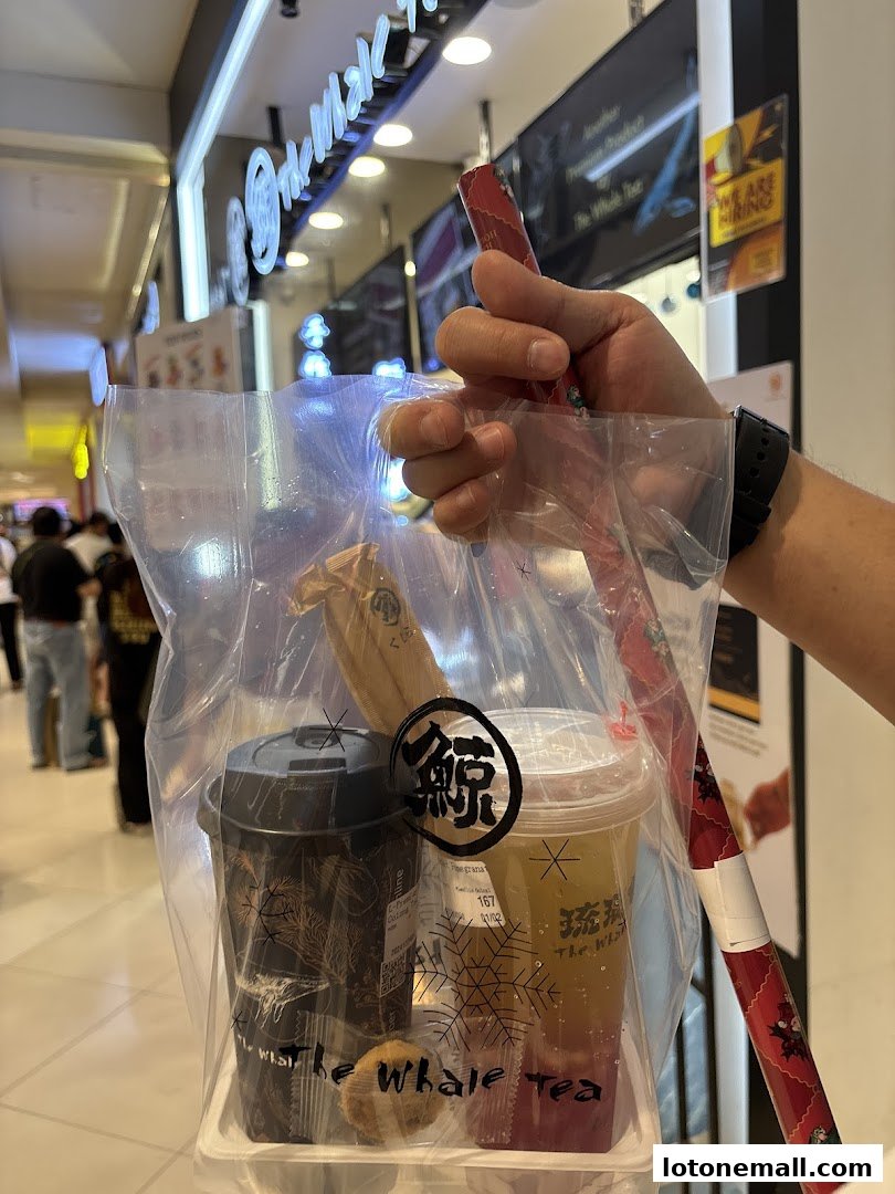 A person holds a plastic bag with two drinks from The Whale Tea.