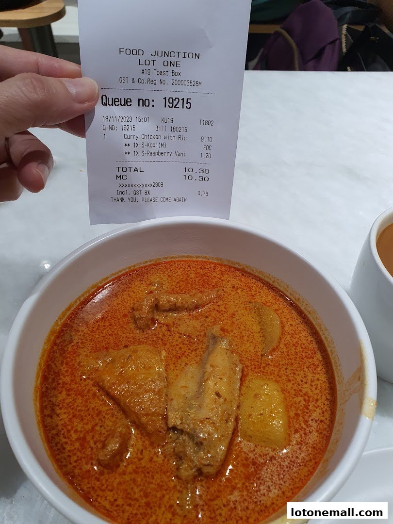 A close-up of a bowl of curry chicken with rice and a receipt from Toast Box.