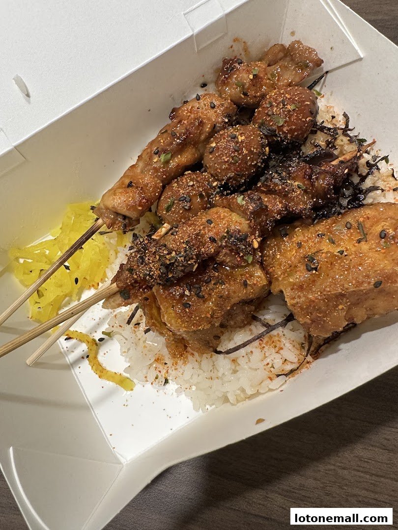 A takeout box filled with rice, various grilled skewers, and pickled vegetables.