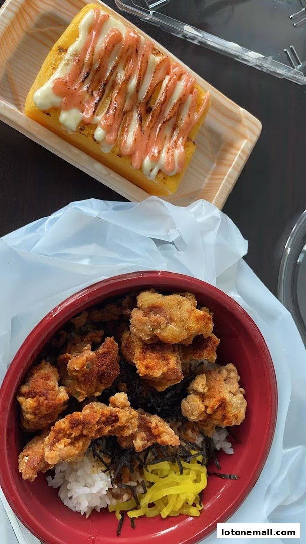 A close-up of Japanese street food, featuring crispy fried chicken over rice and a tamagoyaki with sauce.