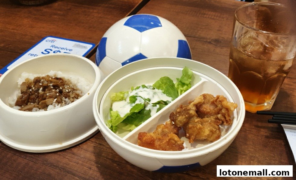 A bento box with rice, salad, and fried chicken, alongside a drink and a soccer ball.